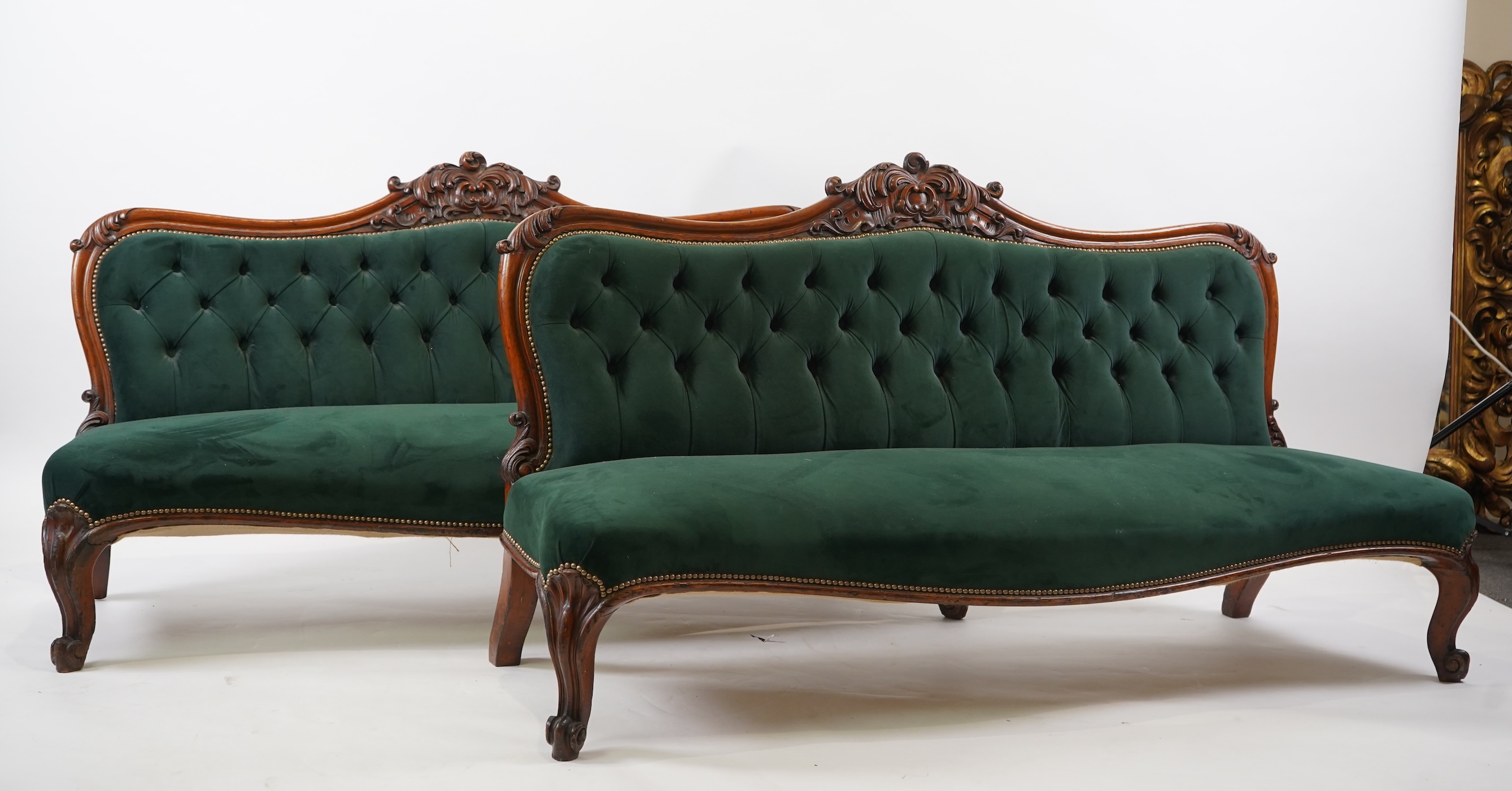 A pair of Victorian carved oak settees, recently re-upholstered in deep buttoned green velvet, the scroll carved crest rails over serpentine seats on cabriole front legs, 160cm wide, 96cm high, Provenance - previously gi